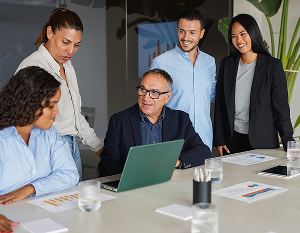 Group of people sitting and standing around a laptop utilizing lean problem solving skills