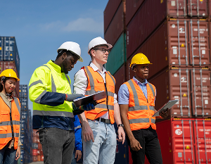 Three diverse men in construction PPE in a shipping container yard, implementing Lean Horizons Academy practices of Strategy Development