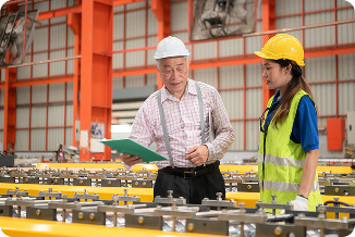 Factory floor workers in PPE. Man in white shirt and hard hat and a women in yellow safety vest and yello hard hat.